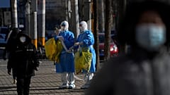 People walk by workers in protective suits look for the location of the lockdown residents to collect COVID samples in Beijing, 1 December 2022