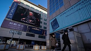 Residents walk by a live broadcast of the memorial service for late Chinese President Jiang Zemin. Tuesday, 6 December 2022.
