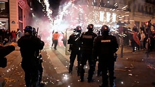 Gendarmes franceses rodeados de fuegos artificiales tras el partido de Marruecos en cuartos de final, en la avenida de los Campos Elíseos, en París, el 10 de diciembre de 2022