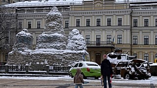 A woman and a child pass by a monument to Princess Olga, covered with sand bags to protect it from shelling, near damaged Russian military vehicles in Kyiv, Dec. 12, 2022.