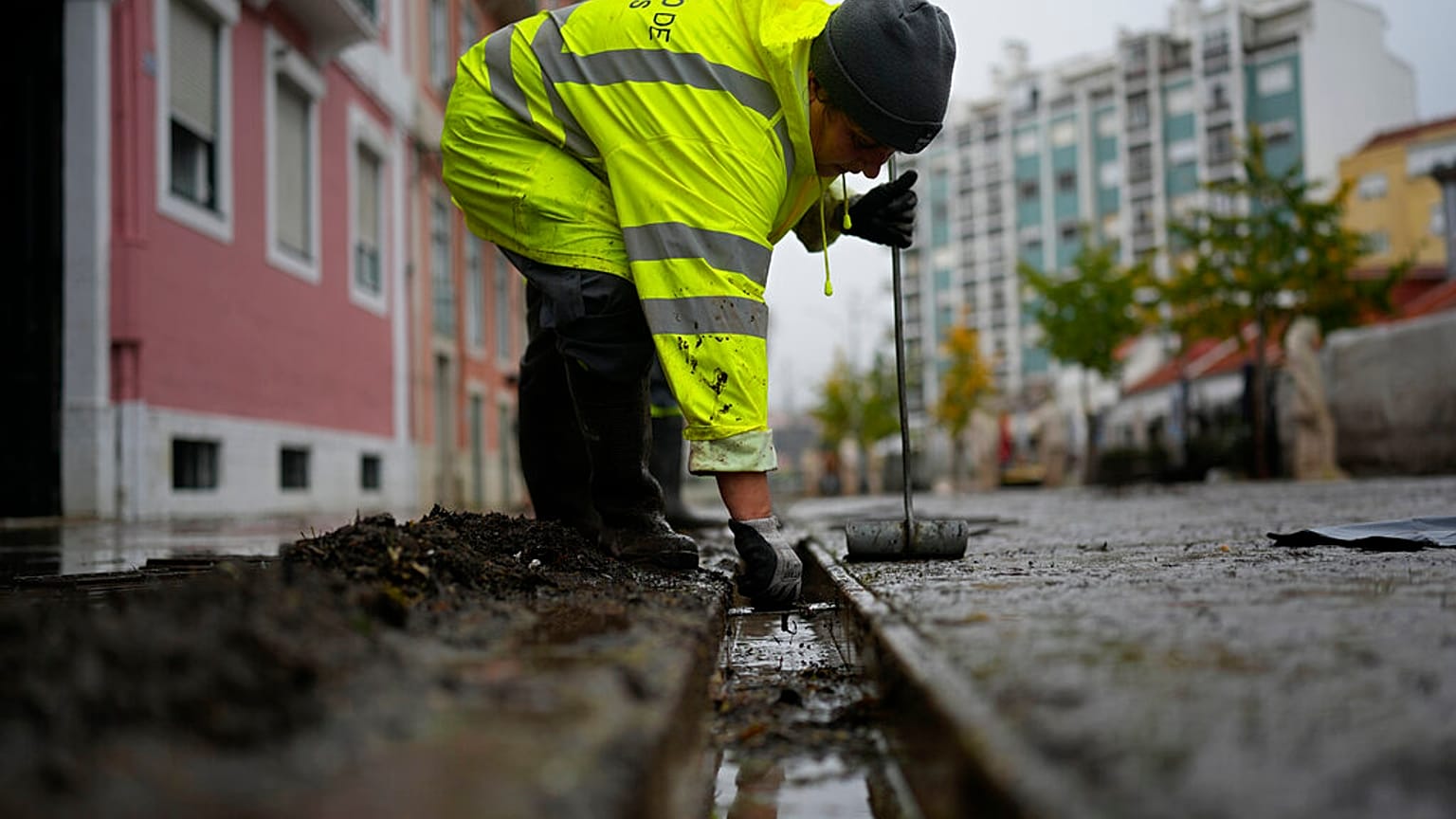 A municipal worker clears the drains in a street that was flooded during heavy rain overnight in Alges, just outside Lisbon, Tuesday, Dec. 13, 2022. 