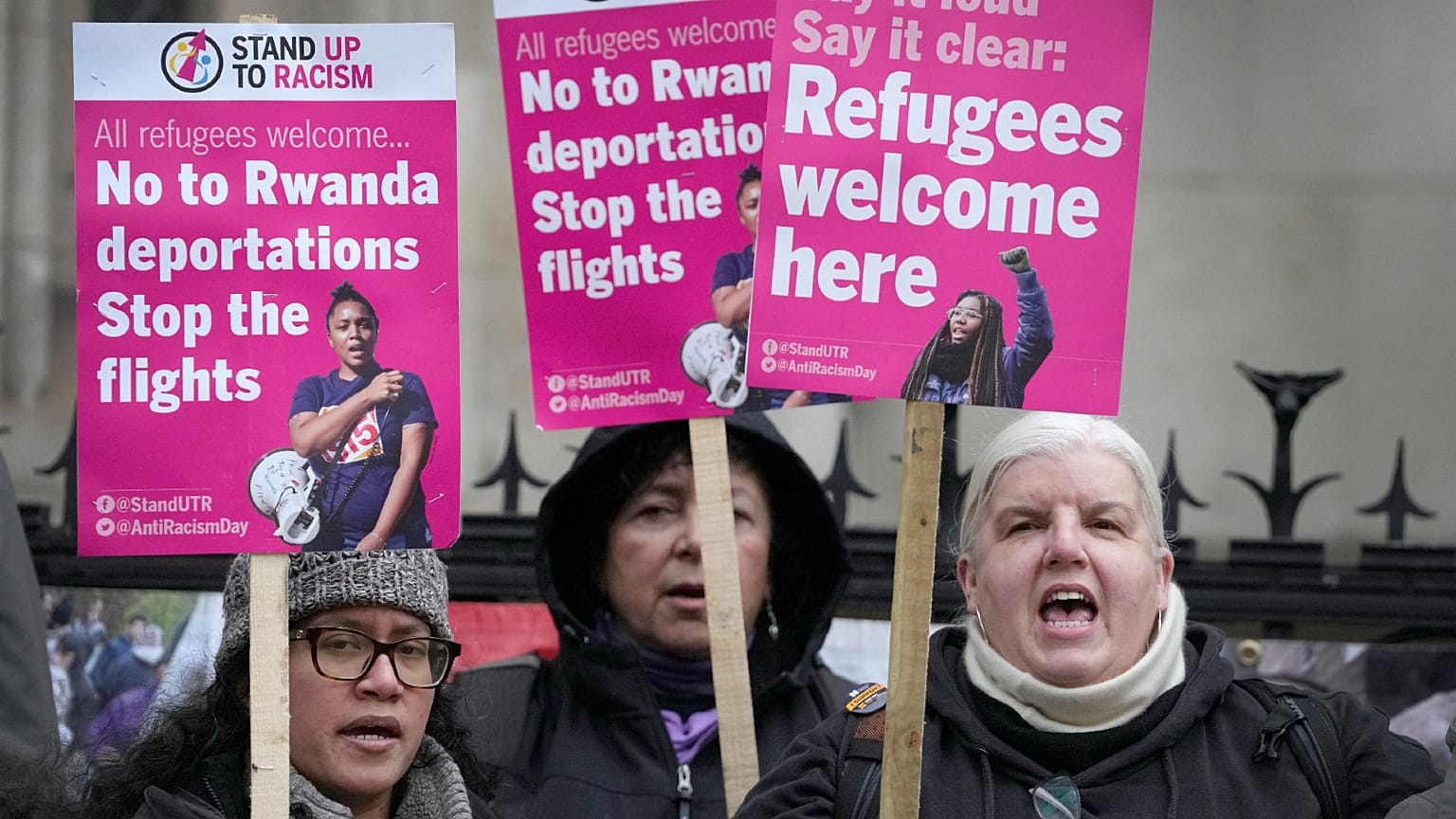 Stand Up To Racism campaigners hold banners outside the High Court in London, Monday, Dec. 19, 2022.