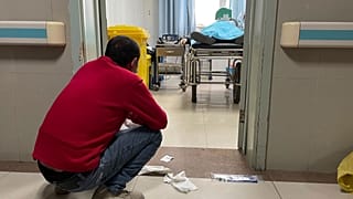 رجل يجلس القرفصاء خارج غرفة العلاج، حيث يتلقى شخص مسن مصاب بـ"كوفيد" المساعدة في التنفس عبر مضخة تهوية في قسم الطوارئ بمستشفى باودينغ بمدينة تشوتشو، شمال الصين، 21 ديسمبر 2022