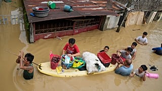 Residents give away onions and other foods along a flooded road due to Typhoon Noru in San Miguel town, Bulacan province, Philippines.