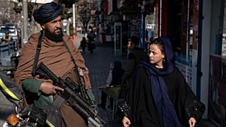 A Taliban fighter stands guard as a woman walks past in Kabul, Afghanistan
