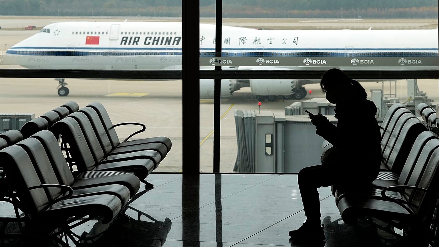 A passenger checks her phone as an Air China jet taxies past at the Beijing Capital International airport in Beijing, 29 October 2022