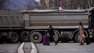 Pedestrians walk past a new road barricade set up in the divided town of Mitrovica on December 28, 2022.