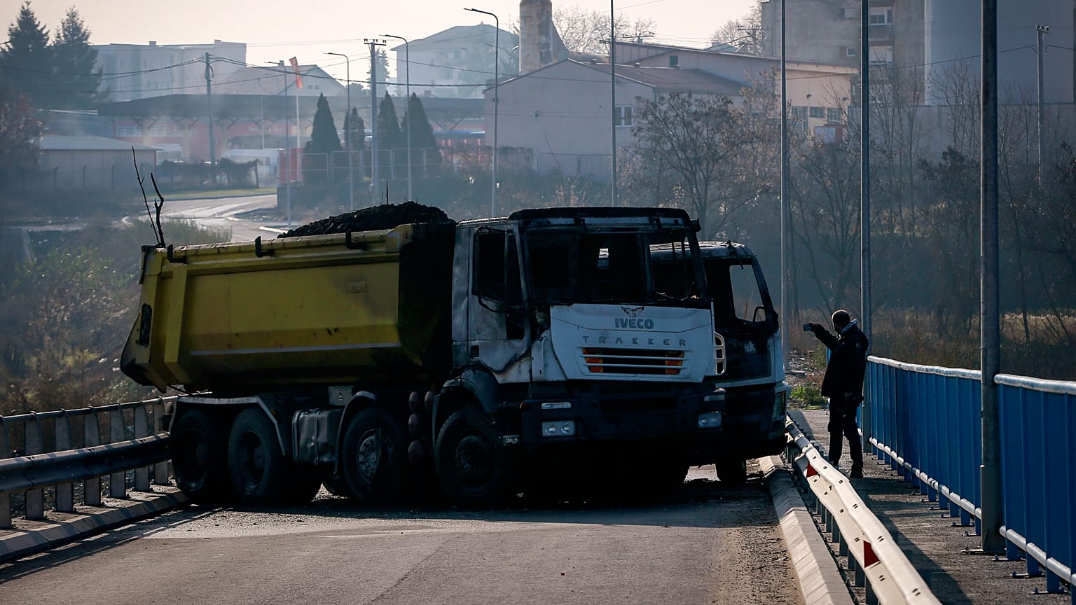 A man takes photos of a burnt-out truck, part of a barricade on the bridge. 