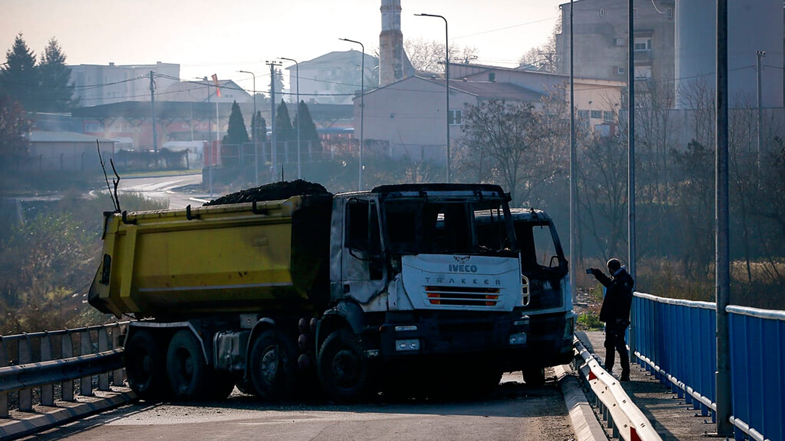 Um homem tira fotografias de um camião queimado, parte de uma barricada, na ponte perto da cidade de Mitrovica, Kosovo