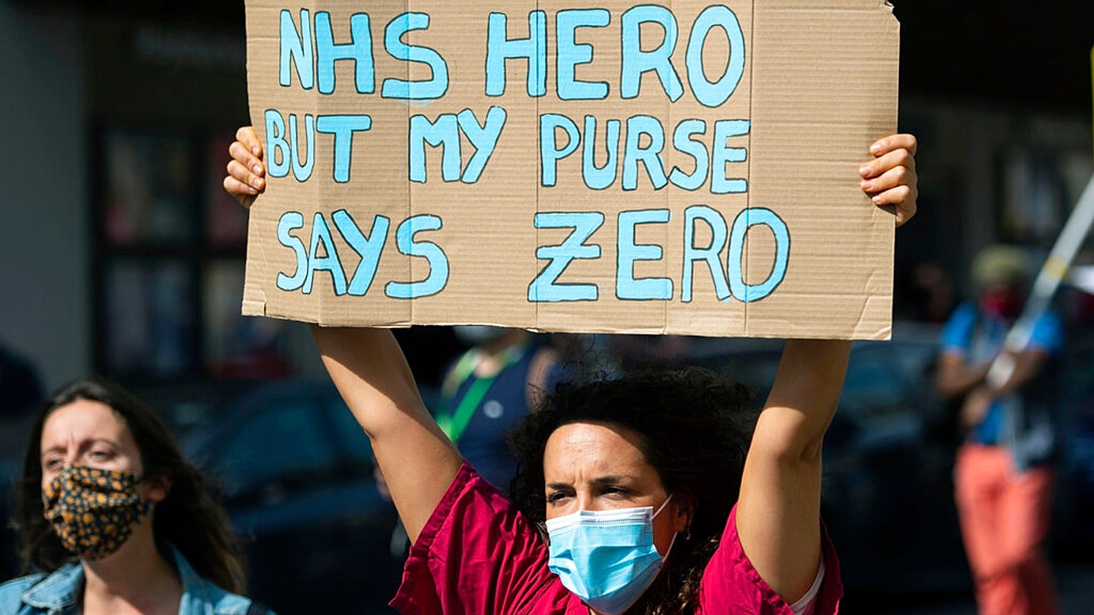 Tüntető tart magasra egy táblát a 2020 szeptemberében tartott, az NHS dolgozóinak követelt béremelések miatti demonstrációk egyikén