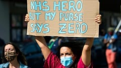 Tüntető tart magasra egy táblát a 2020 szeptemberében tartott, az NHS dolgozóinak követelt béremelések miatti demonstrációk egyikén