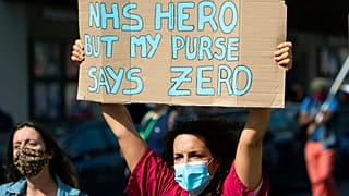 Tüntető tart magasra egy táblát a 2020 szeptemberében tartott, az NHS dolgozóinak követelt béremelések miatti demonstrációk egyikén