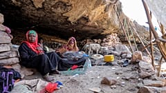 نساء وأطفال في اليمن يجلسون على الأرض في كوخ بجوار كهف حيث لجأت عائلة إلى مأوى بسبب الفقر ونقص السكن.