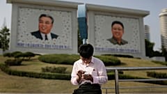 Észak-koreai férfi telefonozik Kim Ir Szen és Kim Dzsong Il portréja előtt