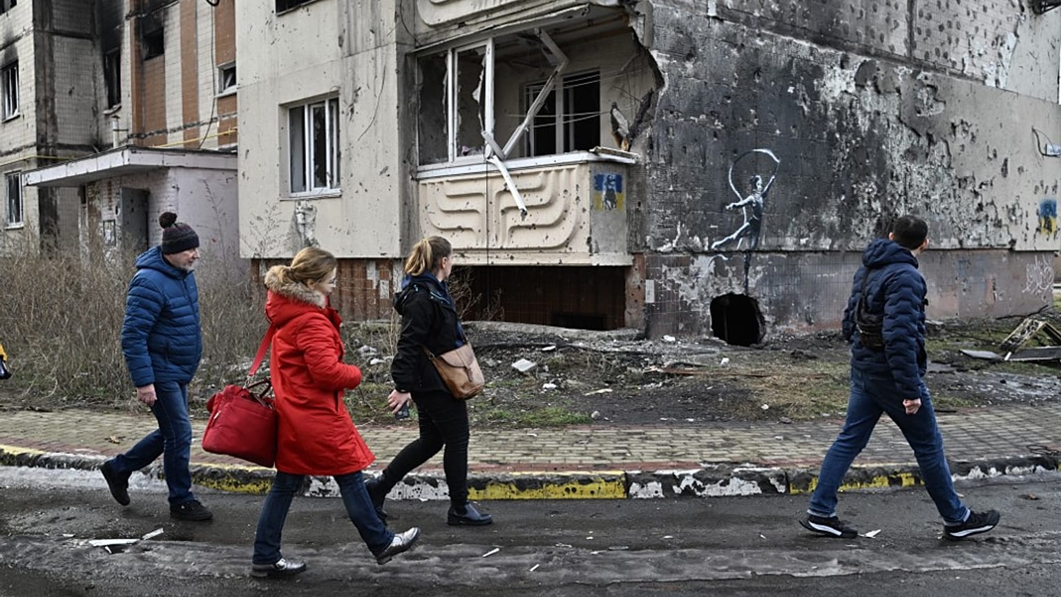 People walk past a Banksy’s graffiti on a wall of a heavily damaged residential building in Irpin, Kyiv, on December 23, 2022, amid the Russian invasion of Ukraine