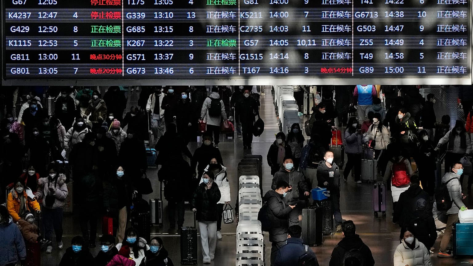Travellers with their luggage walk beneath a trains departure board at the West Railway Station in Beijing.