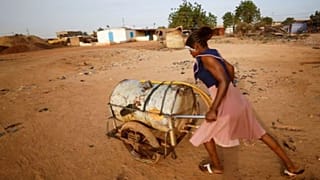 A woman pushes a barrel filled with water on the outskirts of Ouagadougou, Burkina Faso