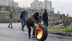 متظاهر فلسطيني يلقي بإطار محترق على قوات الأمن الإسرائيلي وسط مواجهات عند المدخل الشمالي لمدينة رام الله بالقرب من مستوطنة بيت إيل الإسرائيلية، في 20 ديسمبر 2022 