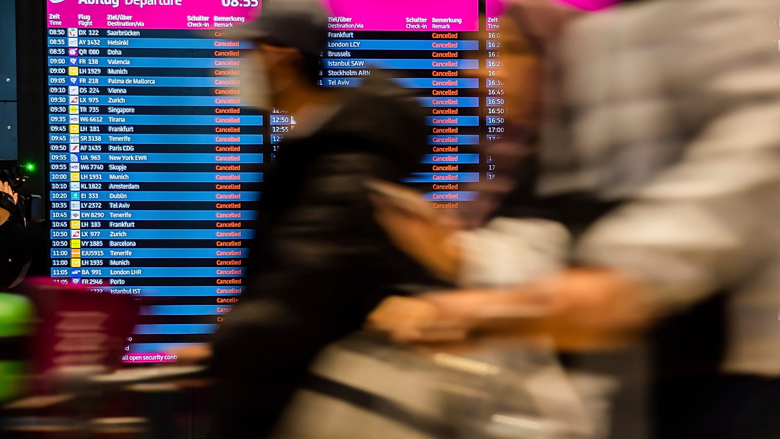 Passengers walk past the display board showing all flights as canceled during a warning strike at Berlin-Brandenburg BER Airport in Schoenefeld, Germany, Jan. 25, 2023