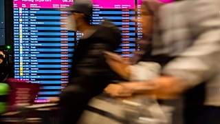 Passengers walk past the display board showing all flights as canceled during a warning strike at Berlin-Brandenburg BER Airport in Schoenefeld, Germany, Jan. 25, 2023