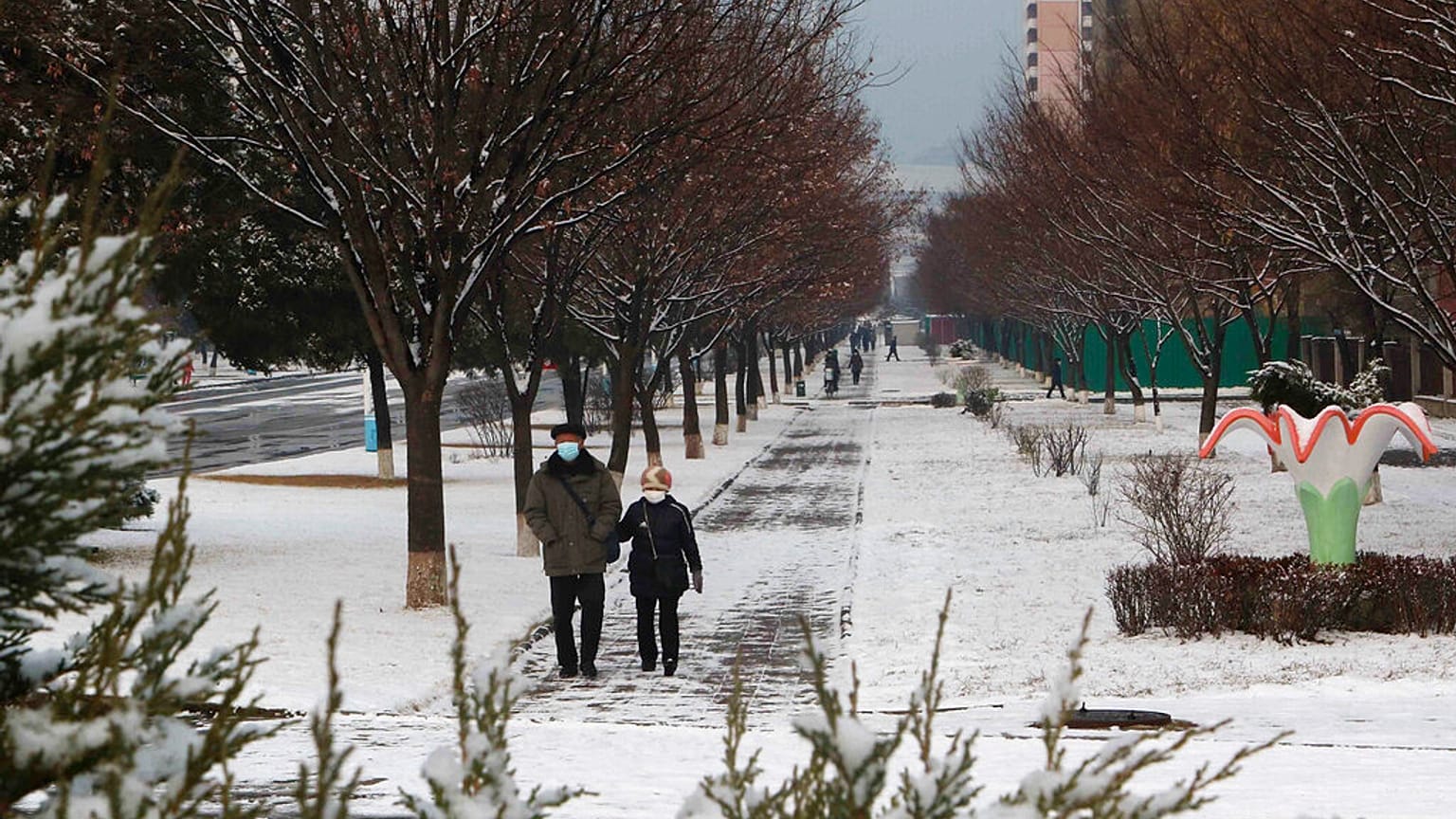 Kuzey Kore'nin başkenti Pyongyang'ın Pothonggang bölgesinde karlı bir caddede yürüyen vatandaşlar 