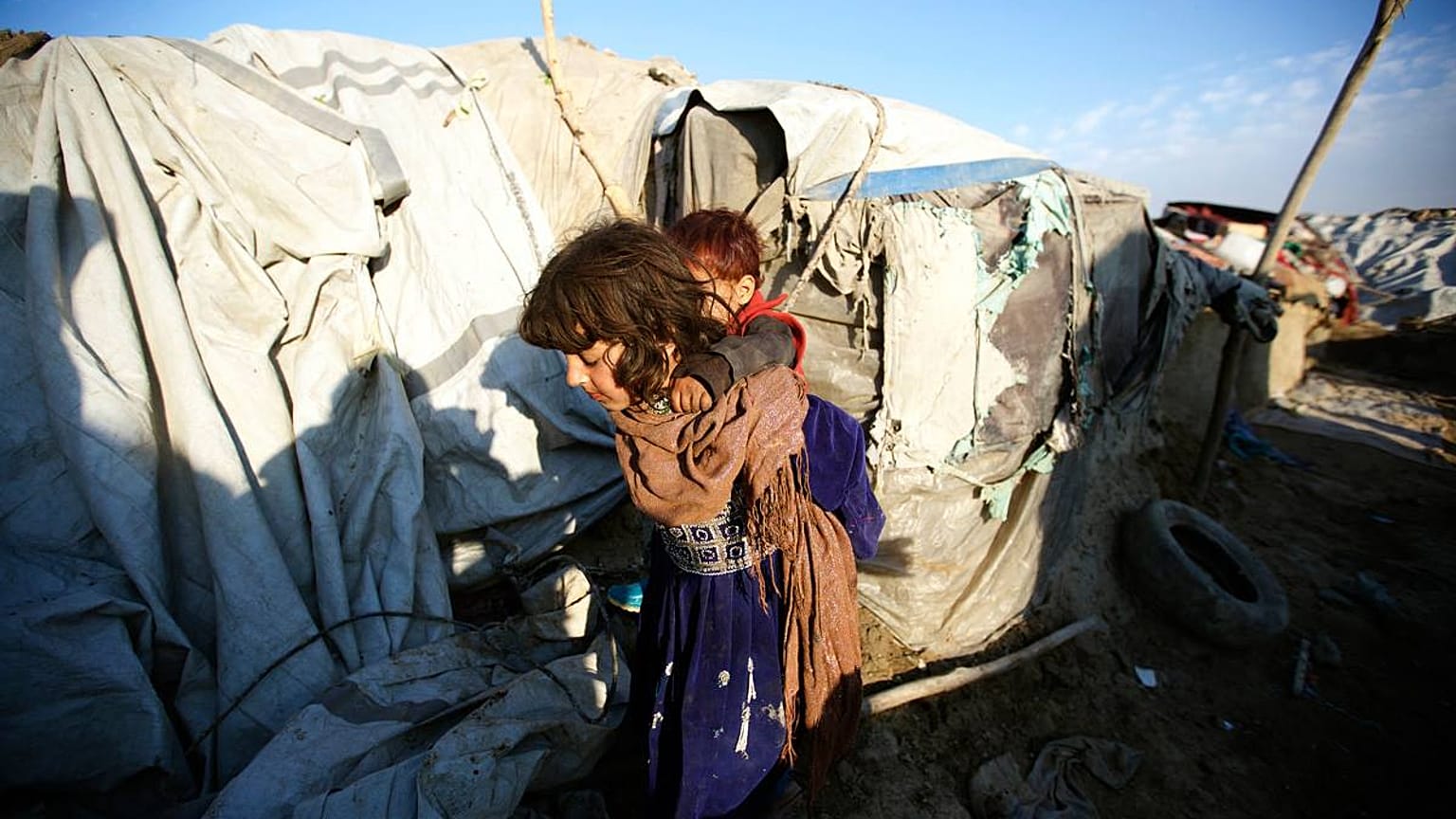 Afganistan'ın başkenti Kabil'e yakın mesafedeki Teymeni mülteci kampında, kardeşini sırtına alan bir kız çocuğu