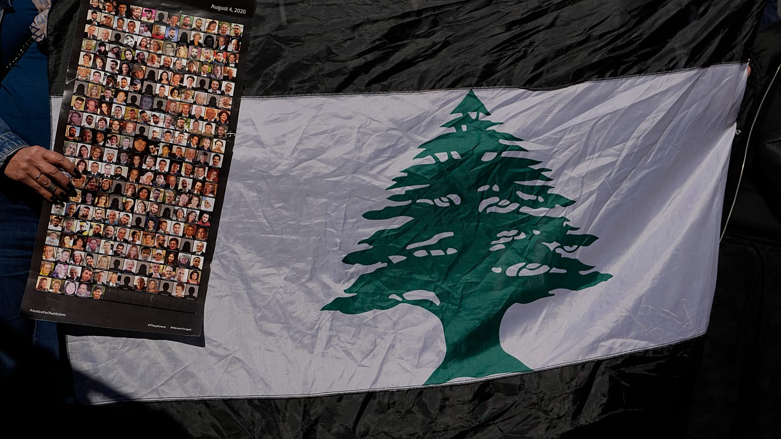 لبنانية تحمل صوراً لضحايا انفجار مرفأ بيروت 2020 بجانب العلم اللبناني خلال احتجاج أمام قصر العدل، بيروت، لبنان 2023