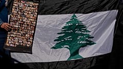 لبنانية تحمل صوراً لضحايا انفجار مرفأ بيروت 2020 بجانب العلم اللبناني خلال احتجاج أمام قصر العدل، بيروت، لبنان 2023