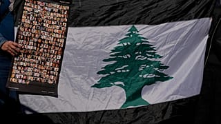 لبنانية تحمل صوراً لضحايا انفجار مرفأ بيروت 2020 بجانب العلم اللبناني خلال احتجاج أمام قصر العدل، بيروت، لبنان 2023