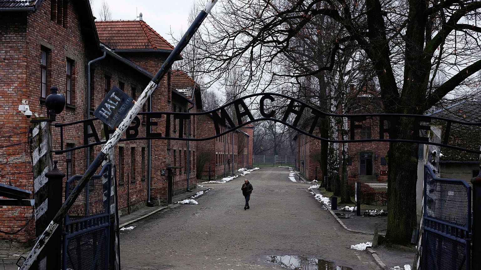 مردی در کنار دروازه "Arbeit Macht Frei" (کار شما را آزاد می کند) در اردوگاه کار اجباری و کشتار آلمان نازی سابق آشویتس-بیرکناو در لهستان، پنجشنبه، ۲۶ ژانویه ۲۰۲۳ 