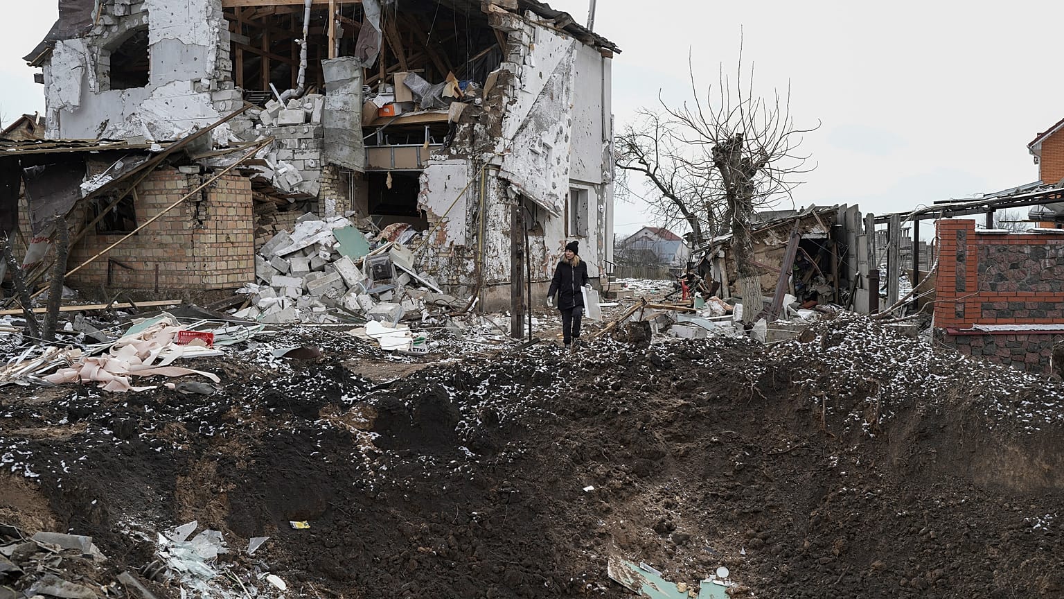 Una mujer sobre un cráter junto a una casa destruida tras un ataque ruso con cohetes en Hlevakha, en la región ucraniana de Kiev, el jueves 26 de enero de 2023.