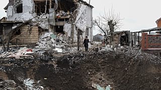 Una mujer sobre un cráter junto a una casa destruida tras un ataque ruso con cohetes en Hlevakha, en la región ucraniana de Kiev, el jueves 26 de enero de 2023.