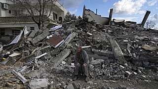 A survivor sits amid the rubble of a collapsed buildings in the town of Nurdagi, Eastern Turkey.