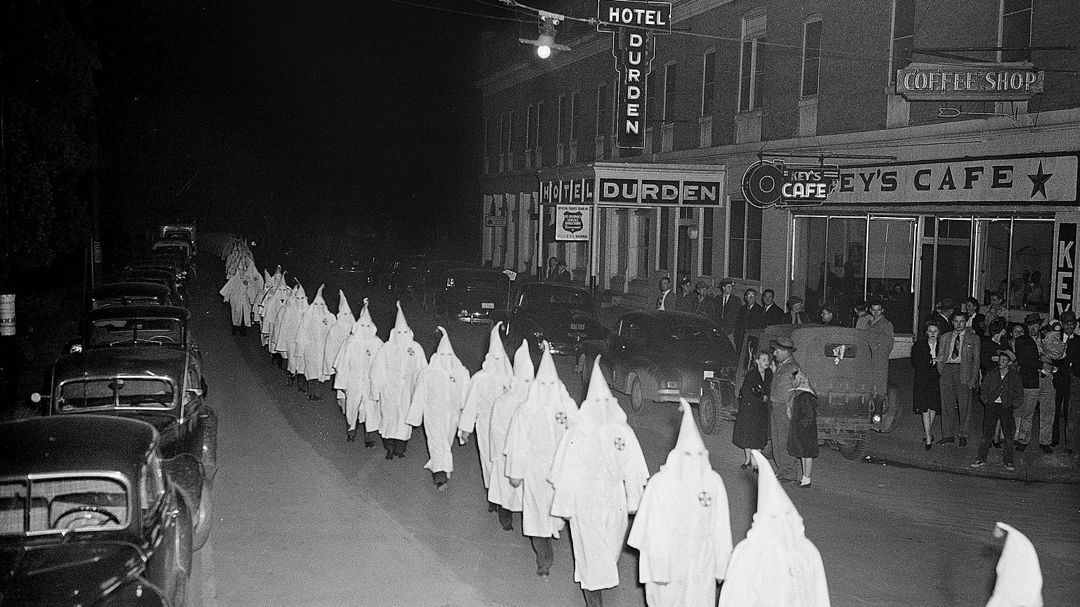 Members of the Ku Klux Klan, wearing traditional white hoods and robes, march in single file 