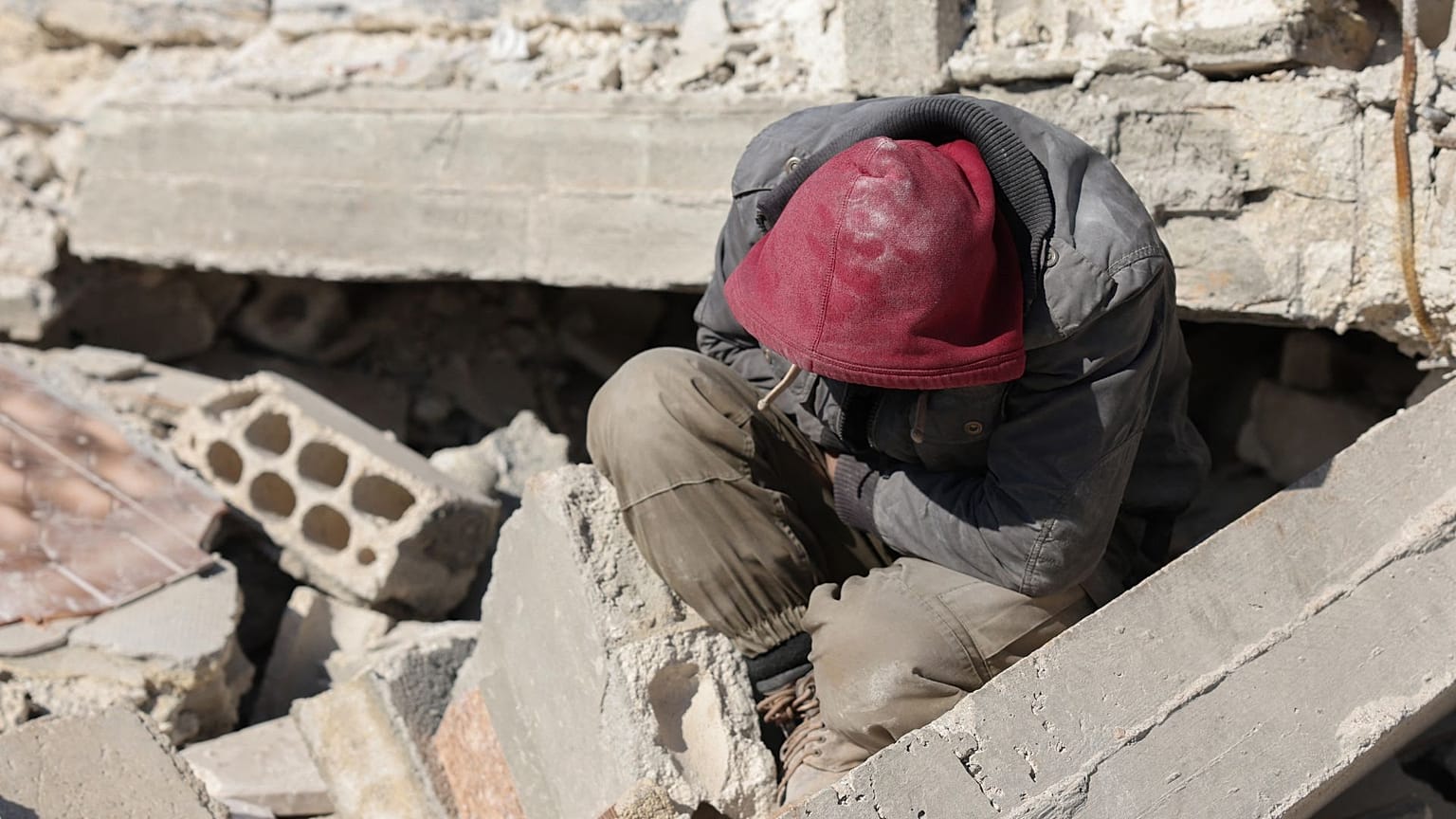 A Syrian man sits amidst the rubble as he waits for new about family members stuck under the wreckage in the town of Harim in Syria.