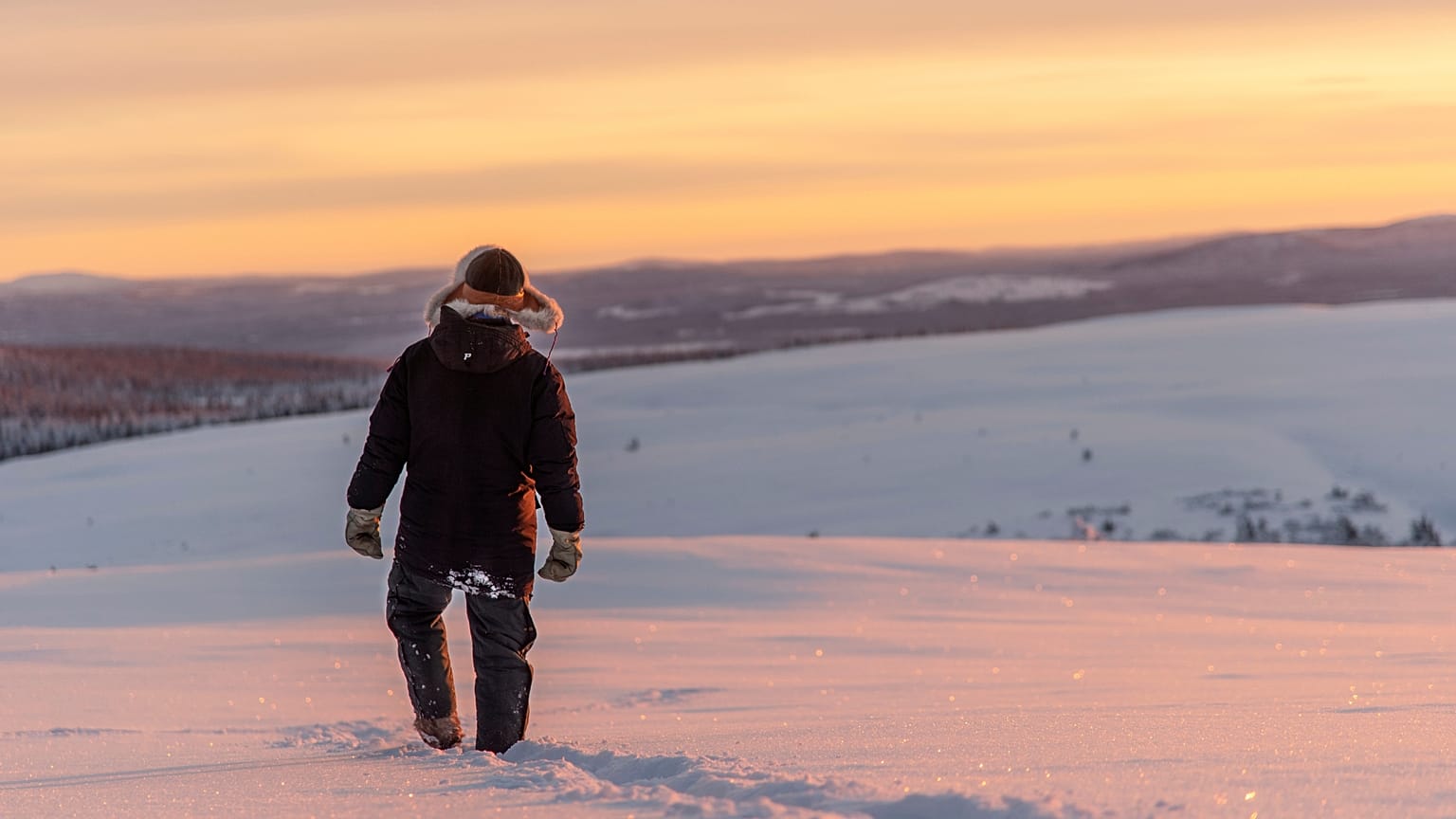 A reindeer herder walks across the snow as the sun sets near Kiruna, Sweden. 