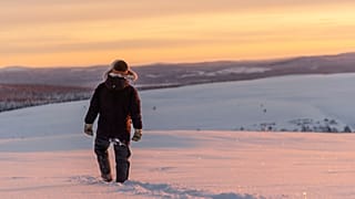 A reindeer herder walks across the snow as the sun sets near Kiruna, Sweden.