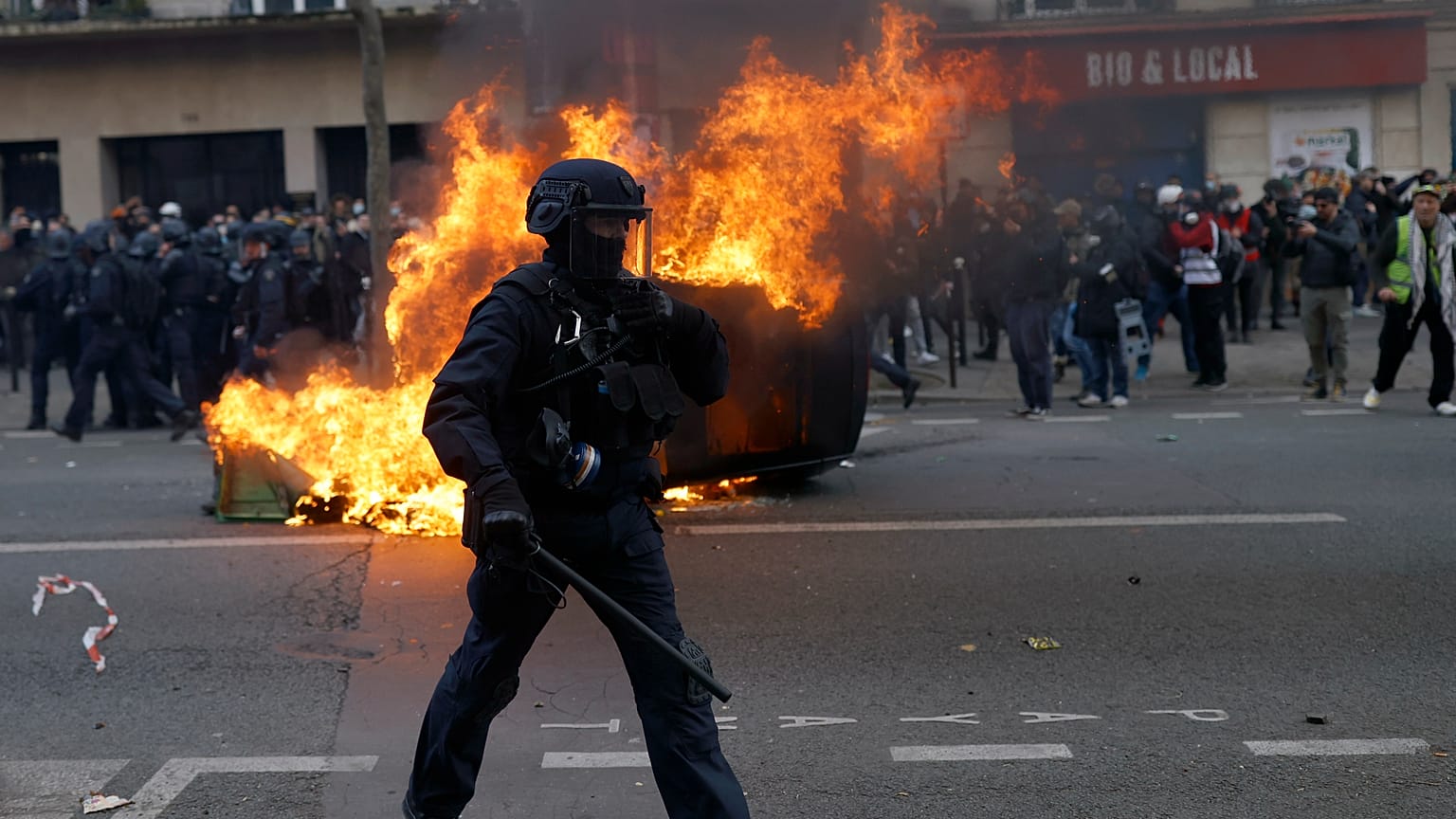 A francia kormány tervezett nyugdíjreformja ellen tüntetők által felgyújtott autó előtt egy rohamrendőr Párizsban 2023. február 11-én.