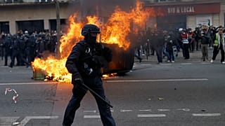 A francia kormány tervezett nyugdíjreformja ellen tüntetők által felgyújtott autó előtt egy rohamrendőr Párizsban 2023. február 11-én.