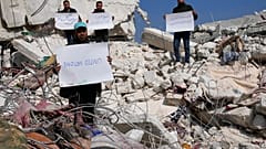 Des Syriens se tiennent au milieu des décombresavec des pancartes critiquant l'ONU, 12 février 2023. 