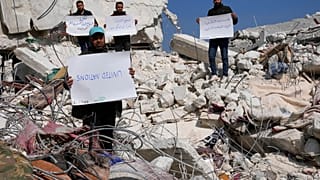 Des Syriens se tiennent au milieu des décombresavec des pancartes critiquant l'ONU, 12 février 2023. 