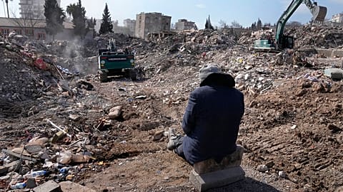 A man watches excavators remove rubble from his building in Kahramanmaras city, southern Turkey, Wednesday, Feb. 15, 2023.