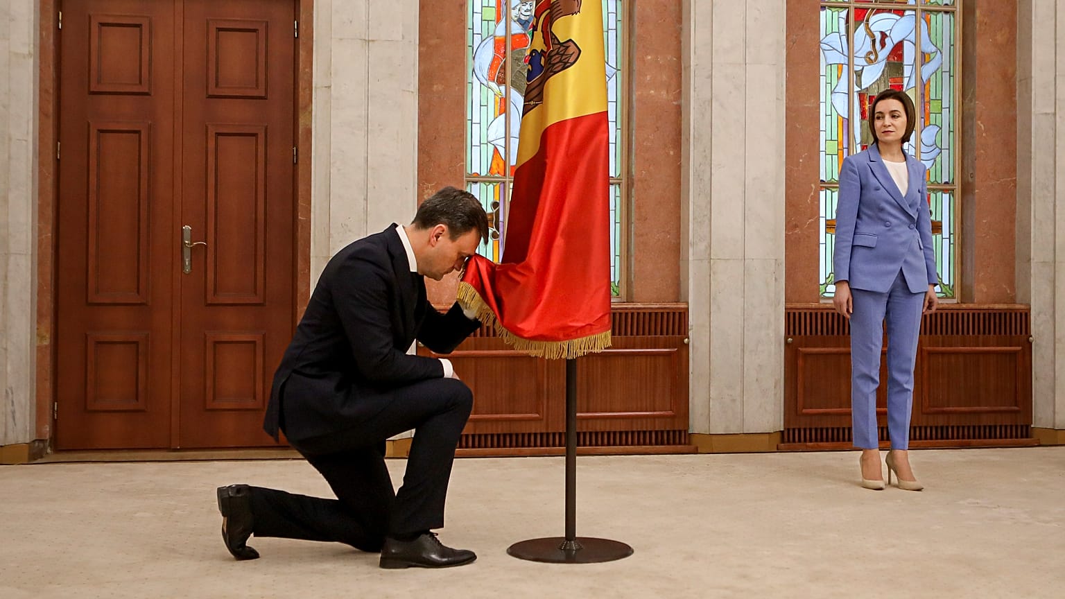 Az új miniszterelnök, Dorin Recean a moldáv zászló előtt térdel beiktatása közben