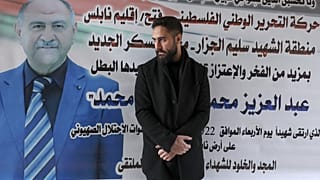 الممرض الفلسطيني إلياس الأشق بجانب لوحة إعلانية عليها نعي لوالده عبد العزيز، 24 فبراير 2023