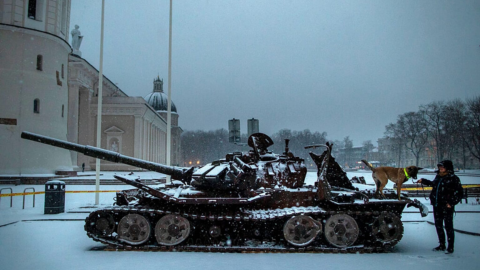 A woman plays with a dog on the destroyed Russian tank t Cathedral Square in Vilnius, Lithuania, Friday, Feb. 24, 2023. 