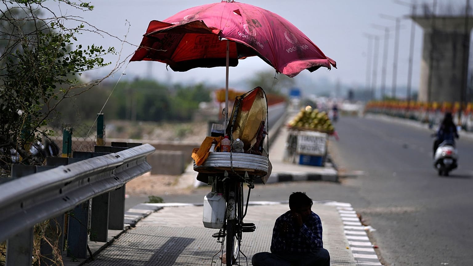 A snacks vendor sits under a shade and waits for customer on a hot summer afternoon in Jammu, India, May 19, 2022. 