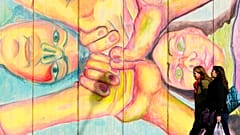 Two women walk past a mural that depicts two women holding hands in Belgrade, Serbia.