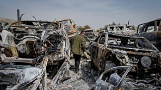 A Palestinian man walks between scorched cars in a scrapyard, in Hawara, near Nablus, West Bank