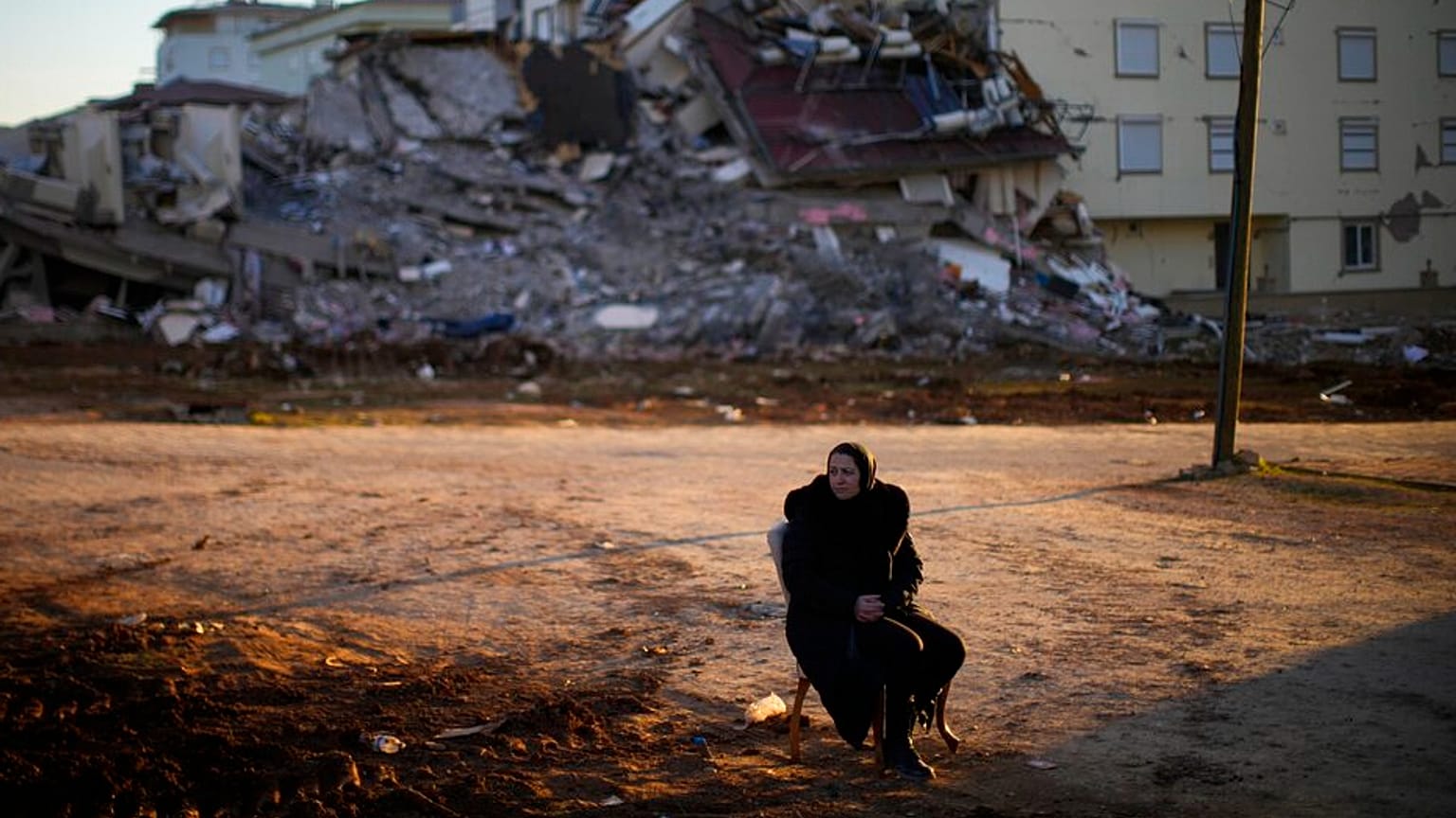 A woman sits on a chair as she waits for her belongings to take away from a damaged building in Pazarcik, Turkey, Monday, Feb. 13, 2023. 