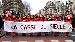 Manifestantes com máscaras do presidente francês Emmanuel Macron seguram faixa onde se lê "O roubo do século", esta terça-feira, em Paris